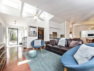 Spacious living room with vaulted ceilings, skylights, leather sofas, and an open-plan kitchen in the background